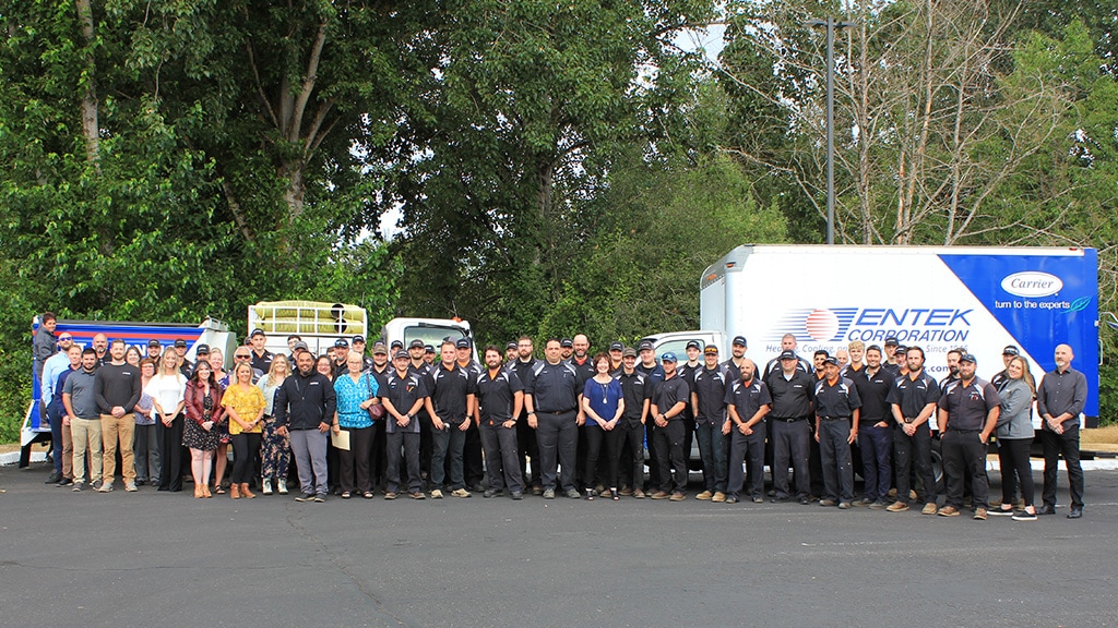 The Entek Corporation team outside lined up outside in front of their service trucks with large trees with green leaves behind them in the background.