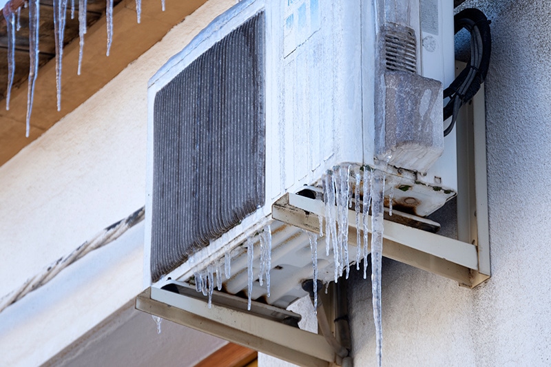 Why Is My Heat Pump Freezing Up? Image is a photograph of a frozen heat pump on a home's exterior.