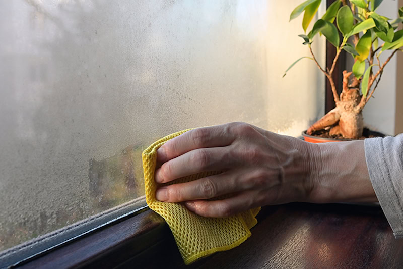 hand wiping away condensation from a window at home.